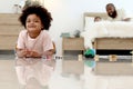 Portrait of happy smiling African boy with black curly hair lying on floor, playing toy in bedroom. Child with reflections on Royalty Free Stock Photo