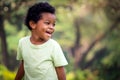 Portrait of happy smiling African boy with black curly hair standing and laughing outdoor with blurred green garden background, Royalty Free Stock Photo