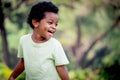 Portrait of happy smiling African boy with black curly hair standing and laughing outdoor with blurred green garden background, Royalty Free Stock Photo