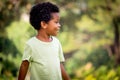Portrait of happy smiling African boy with black curly hair standing and laughing outdoor with blurred green garden background, Royalty Free Stock Photo