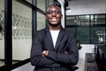 Portrait of happy smiling African businessman in black suit wearing glasses and standing with arms crossed inside building Royalty Free Stock Photo