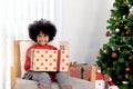 Portrait of happy smiling African kid girl with curly hair sitting on chair, holding Christmas gift box present with beautiful Royalty Free Stock Photo