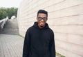 Portrait happy smiling african man in black hoodie, sunglasses on city street over gray brick wall Royalty Free Stock Photo