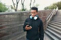 Portrait happy smiling african man with phone, headphones listening to music wearing black hoodie, walking on city Royalty Free Stock Photo