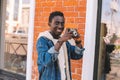 Portrait happy smiling african man with vintage film camera taking picture walking on city street over brick wall Royalty Free Stock Photo