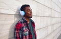 Portrait happy smiling african man in wireless headphones enjoying listening to music on city street over gray wall Royalty Free Stock Photo