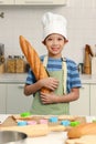 Portrait of Happy smiling Asian boy with apron and chef hat, holding baguette French bread while standing at kitchen, cute child Royalty Free Stock Photo