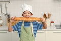 Portrait of Happy smiling Asian boy with apron and chef hat, holding baguette French bread while standing at kitchen, cute child Royalty Free Stock Photo