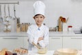 Portrait of happy smiling Asian boy in white chef uniform with hat standing with arms crossed and mixing eggs bowl on table at Royalty Free Stock Photo