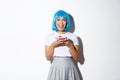 Portrait of happy smiling asian girl with cute makeup, wearing blue short wig, holding piece of cake, standing over