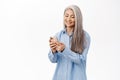 Portrait of happy smiling asian woman, old lady using smartphone app, holding mobile phone in hands, standing over white Royalty Free Stock Photo