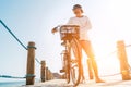 Portrait of a happy smiling barefoot man dressed in light summer clothes and sunglasses riding a bicycle on the wooden sea pier.