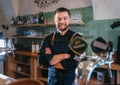 Portrait of happy smiling bearded barman dressed in a black uniform with an apron at bar counter with draught beer taps. Royalty Free Stock Photo