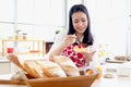 Portrait of happy smiling beautiful Asian woman in red heart apron spreading jam on slices of toast bread while sitting behind Royalty Free Stock Photo