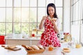 Portrait of happy smiling beautiful Asian woman in red heart apron spreading jam on slices of toast bread while standing behind Royalty Free Stock Photo