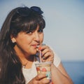 Portrait of happy smiling beautiful overweight young woman in white T-shirt drinking sweet coffee through a straw outdoors beach Royalty Free Stock Photo