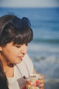 Portrait of happy smiling beautiful overweight young woman in white T-shirt drinking sweet coffee through straw outdoors at beach Royalty Free Stock Photo