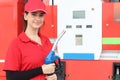 Portrait of happy smiling beautiful woman gas station attendant in red uniform holding a fuel petrol pump nozzle against at gas Royalty Free Stock Photo