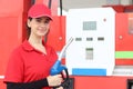 Portrait of happy smiling beautiful woman gas station attendant in red uniform holding a fuel petrol pump nozzle against at gas Royalty Free Stock Photo