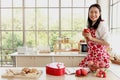 Portrait of happy smiling beautiful young Asian woman in red heart apron holds red coffee mug while stands behind kitchen counter Royalty Free Stock Photo