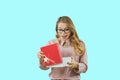 Portrait of a happy smiling blonde girl who opens a gift box with a red lid on a blue isolated background in the studio Royalty Free Stock Photo