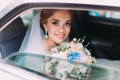 Portrait of the happy smiling bride with the wedding bouquet sitting in the car.