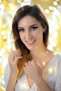 Portrait of a happy smiling brunette young woman wearing white dress in front of blurry golden lights Royalty Free Stock Photo