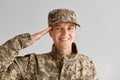 Portrait of happy smiling Caucasian woman army soldier saluting while posing against light background indoor, looking at camera Royalty Free Stock Photo