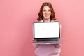 Portrait of happy smiling curly haired teenage girl in hoodie showing empty laptop screen on camera, place for advertisement Royalty Free Stock Photo