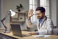 Portrait of happy, smiling doctor sitting at his workplace during online conference using webcam video call on laptop Royalty Free Stock Photo