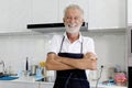 Portrait of happy smiling elderly man with apron standing with arms crosse at kitchen counter. senior man preparing for cooking Royalty Free Stock Photo