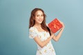 Portrait of a happy smiling girl in dress holding present box and winking isolated over blue background Royalty Free Stock Photo