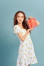 Portrait of a happy smiling girl in dress holding present box and winking isolated over blue background Royalty Free Stock Photo
