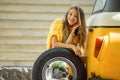 Happy smiling girl is wearing yellow sweater is posing with auto wheel near old retro bus, autumn concept Royalty Free Stock Photo