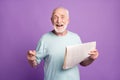 Portrait of happy smiling grey hair beard pensioner hold glasses newspaper wear light blue t-shirt isolated on violate