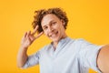 Portrait of happy smiling guy 20s taking selfie photo and showing peace sign, isolated over yellow background Royalty Free Stock Photo