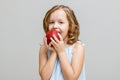 Portrait of a happy smiling little blonde girl on a gray background. Baby bites red apple Royalty Free Stock Photo