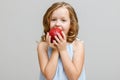 Portrait of a happy smiling little blonde girl on a gray background. Baby bites red apple Royalty Free Stock Photo