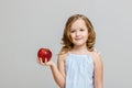 Portrait of a happy smiling little blonde girl on a gray background. The child is holding a red apple Royalty Free Stock Photo