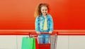 Portrait of happy smiling little girl child with trolley cart and shopping bags wearing denim clothes on city street Royalty Free Stock Photo