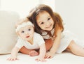 Portrait happy smiling little older and younger sisters together, children playing in white room at home