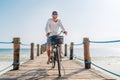 Portrait of a happy smiling man dressed in light summer clothes and sunglasses riding a bicycle on the wooden sea pier. Careless Royalty Free Stock Photo