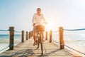 Portrait of a happy smiling man dressed in light summer clothes and sunglasses riding a bicycle on the wooden sea pier. Careless Royalty Free Stock Photo