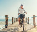 Portrait of a happy smiling man dressed in light summer clothes and sunglasses riding a bicycle on the wooden sea pier. Careless Royalty Free Stock Photo