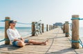 Portrait of a happy smiling man dressed in light summer clothes and sunglasses sitting and enjoying time on wooden sea pier. Royalty Free Stock Photo