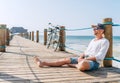 Portrait of a happy smiling man dressed in light summer clothes and sunglasses sitting and enjoying time on wooden sea pier. Royalty Free Stock Photo