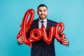 Portrait of happy smiling man wearing official style suit holding love word of foil balloons Royalty Free Stock Photo