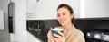 Portrait of happy, smiling modern woman, starts her day with morning mug of tea. Girl drinking coffee in the kitchen Royalty Free Stock Photo