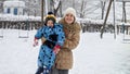 Portrait of happy smiling mother holding her toddler son and walking over snowdrifts on playground after blizzard. Fun and joy on Royalty Free Stock Photo