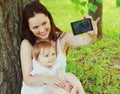 Portrait happy smiling mother taking a selfie by smartphone with her baby on the grass in a summer park Royalty Free Stock Photo